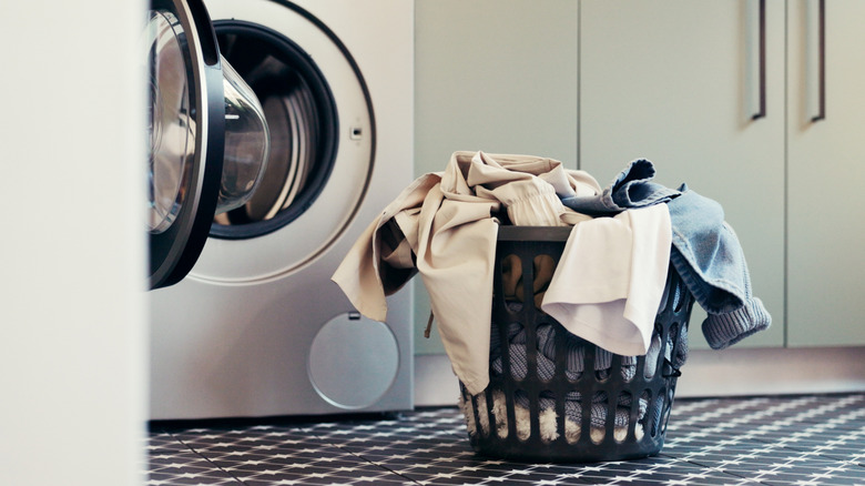 An open dryer with a basket of clothes next to it in a laundry room