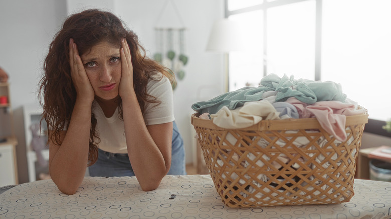 A woman looking frustrated and overwhelmed with a large basket of laundry beside them