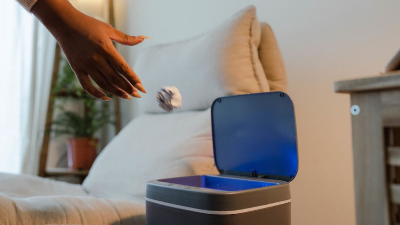 A woman tossing a crumpled ball of paper into a smart trash can