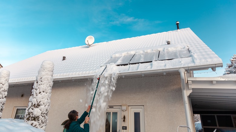 A person uses a telescoping tool to clean snow off roof-mounted solar panels