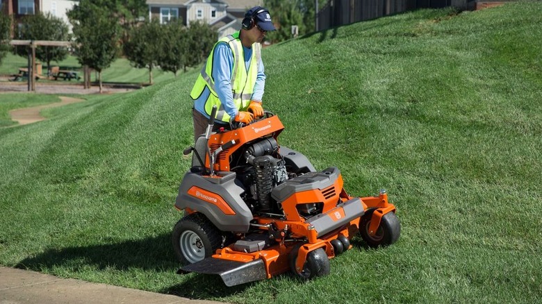 A Husqvarna stand-on lawn mower cutting grass on a sloped yard