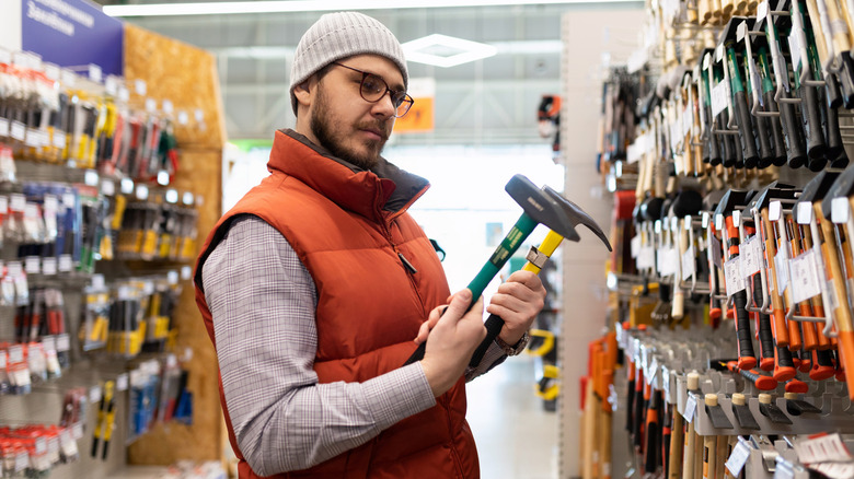 A man compares two hammers in a store