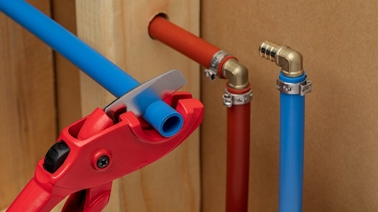 Red tool installing red and blue PEX plumbing in a home