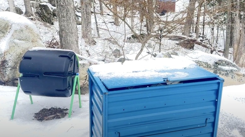 A black plastic tumbling composter outside in a snow-covered backyard.