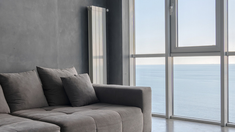 A white vertical radiator behind a gray couch next to a window