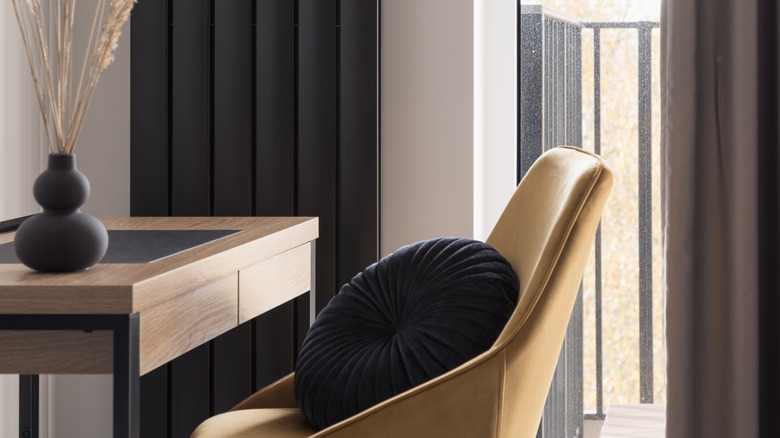 A black vertical radiator behind a table with a vase in the same color
