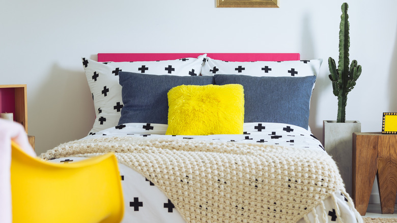 Vibrant bedding with a hot pink headboard, black and white patterned sheets, chambray shams, and a vibrant yellow accent pillow