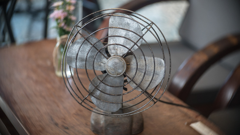 A metal vintage fan on top of a wood table.