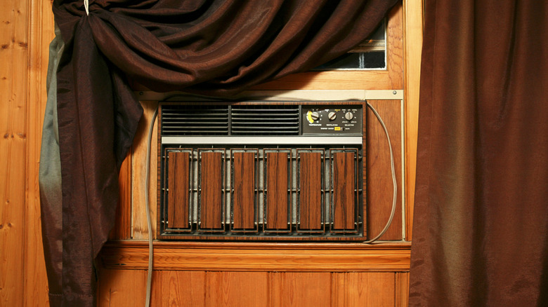 A brown vintage A/C unit behind a brown curtain.