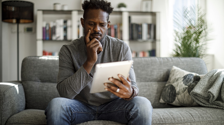 A man sitting on a sofa and looking at his tablet.