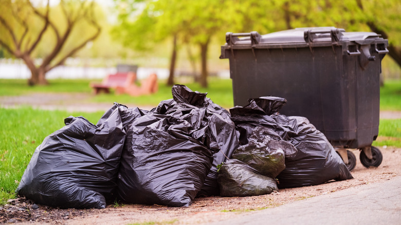 A pile of black garbage bags next to a trash can