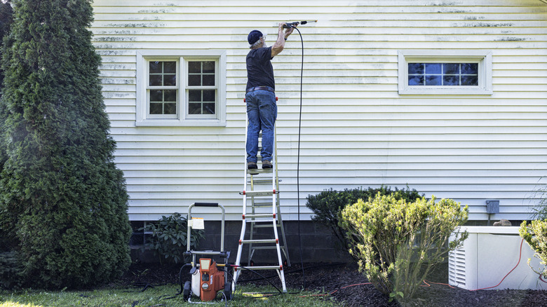 Person pressure washing a house