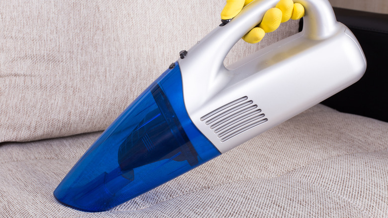 Gloved hand vacuuming sofa with handheld vacuum cleaner