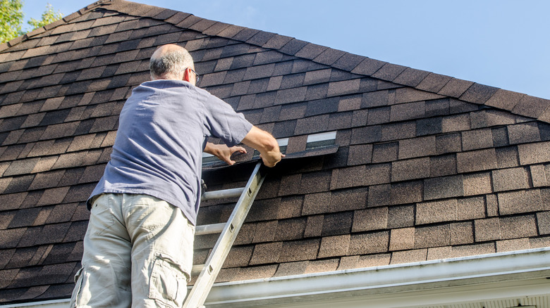 Man on ladder repairing asphalt shingle roof