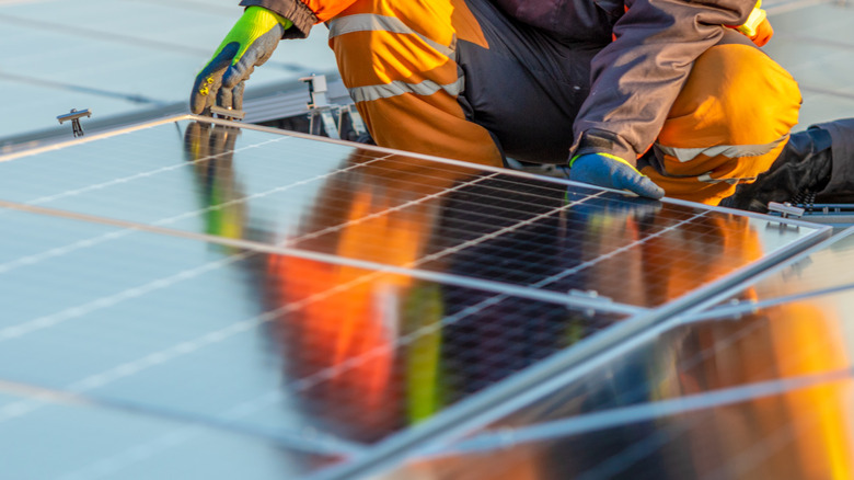 A worker removes old solar panels from a residential rooftop for recycling.