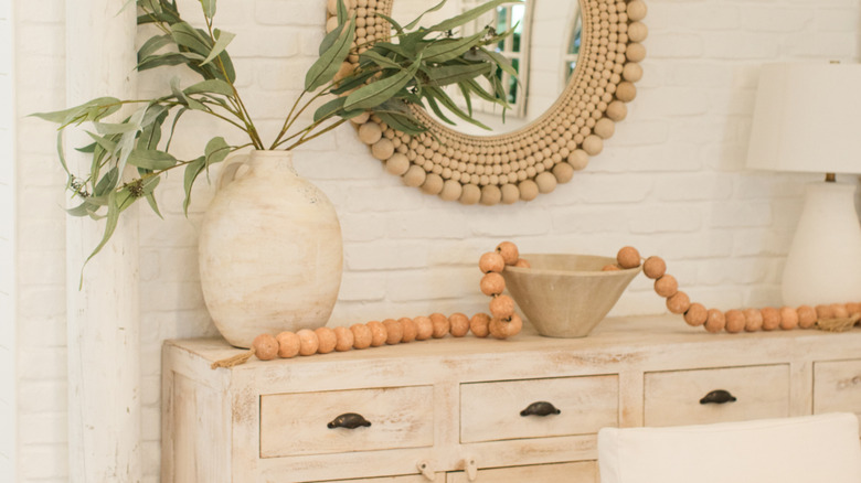 Side console with plant, lamp, and wooden beads in bowl.