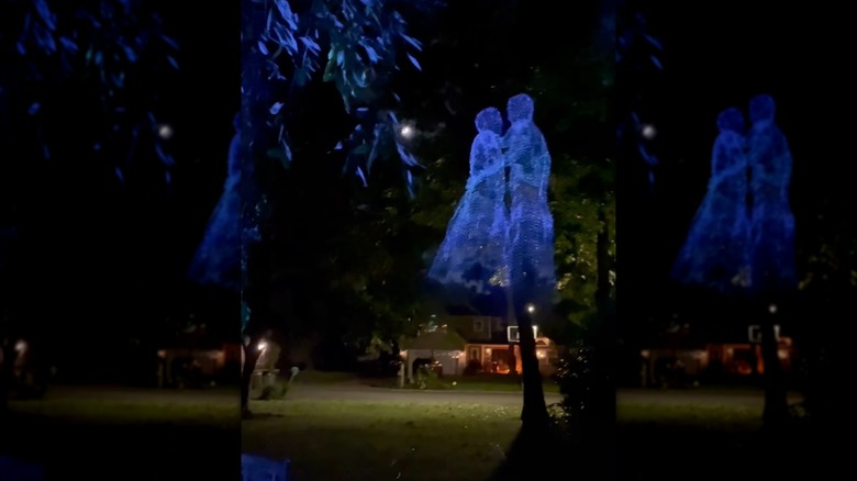 Fake ghost figurines made out of chicken wire posed dancing in a yard at night.