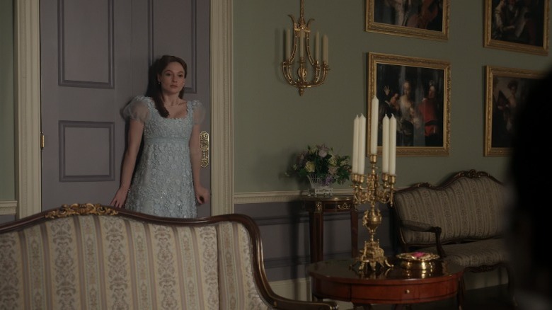 Francesca Bridgerton stands awkwardly against a door in a drawing room.