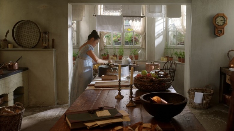 Sophie Baek scrubbing dishes in a Bridgerton kitchen with three wicker baskets
