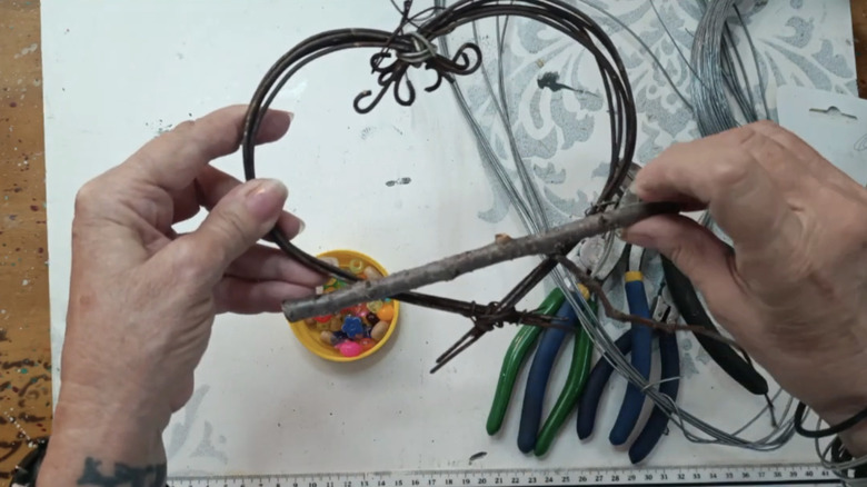 Hands holding a wire heart with a twig perch.
