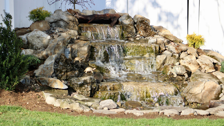 Backyard pondless waterfall feature with stones and shrubbery.
