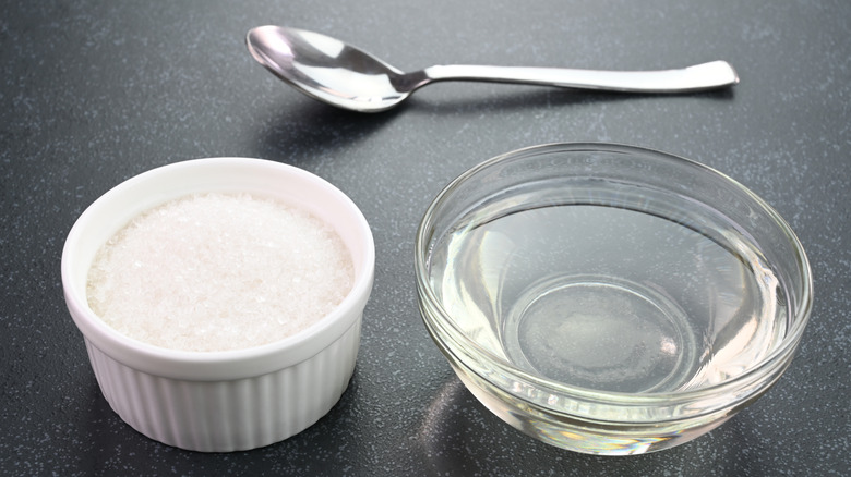 A bowl of sugar and bowl of water sit next to a spoon
