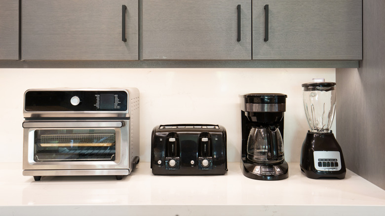 A toaster oven, toaster, coffee machine, and blender sitting in a row on a kitchen counter