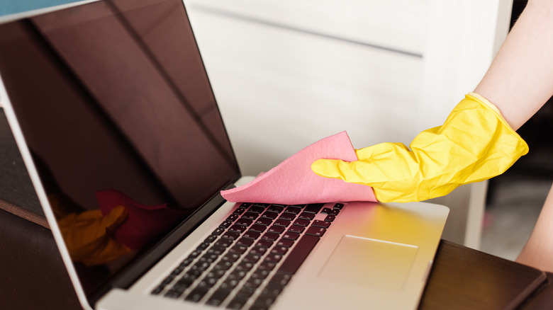 Hand wearing rubber glove cleaning a laptop
