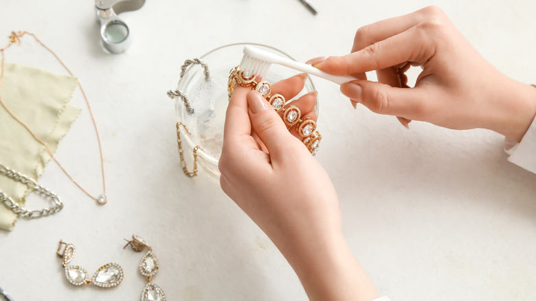 Woman cleaning jewlery in a glass bowl with a tooth brush
