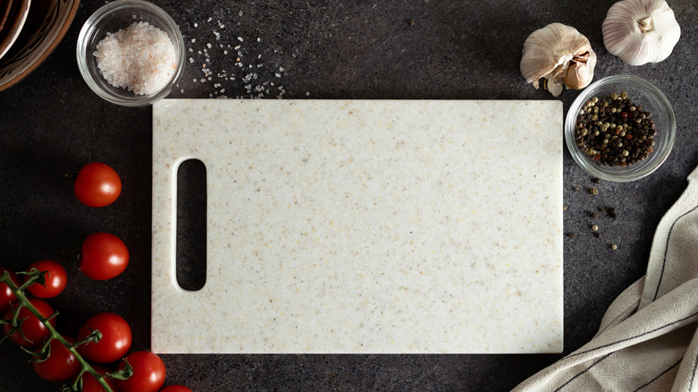 Sone cutting board with tomatoes, salt, pepper, and garlic around it