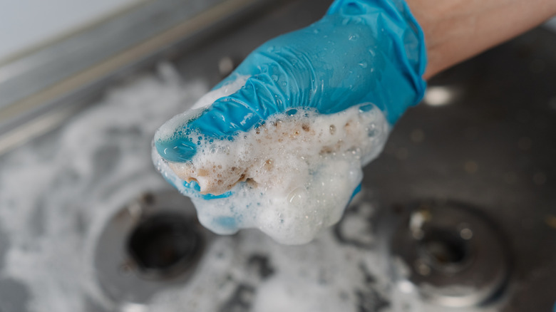 Person with blue gloves cleaning a gas stove with a soapy, wet sponge