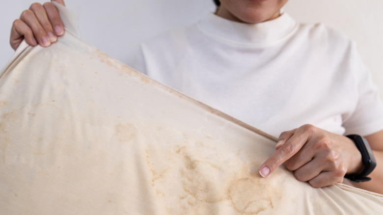 A person holding an old, stained yellow pillow