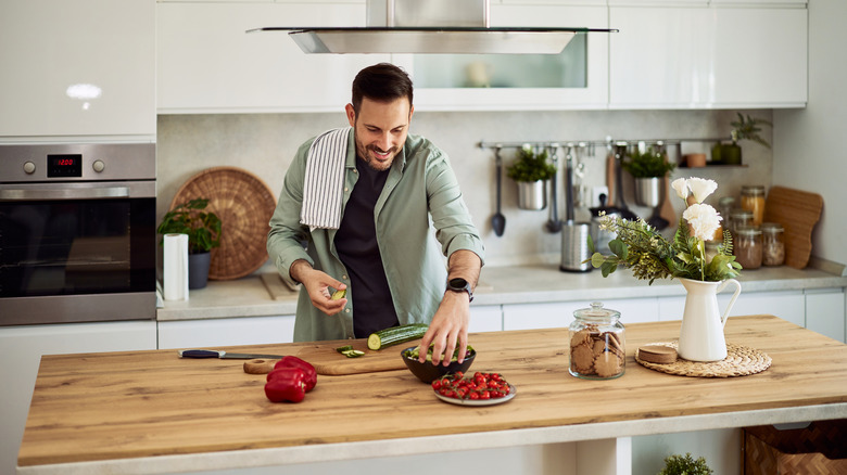 An adult male prepping salad ingredients on wooden kitchen island