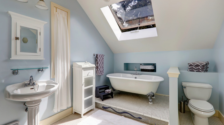 Bathroom with pale, dusty blue paint and white fixtures with a skylight over the tub