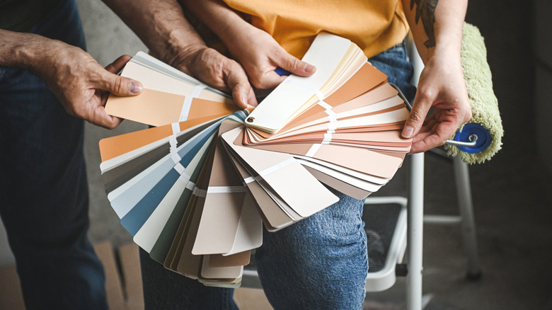 Two people holding a bunch of neutral-toned paint color swatches deciding on a paint color