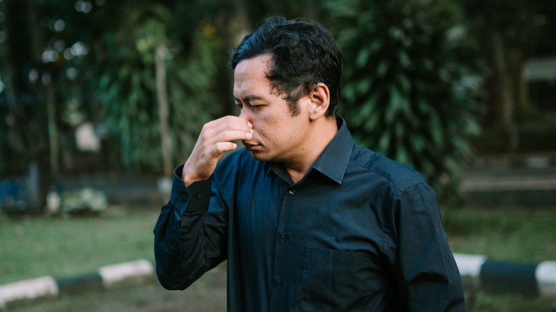 A man standing outside pinching his nose