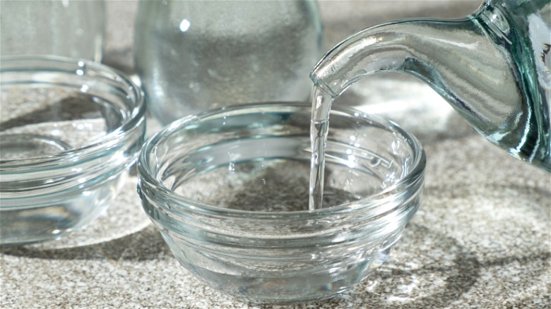 person pouring white vinegar into glass bowl