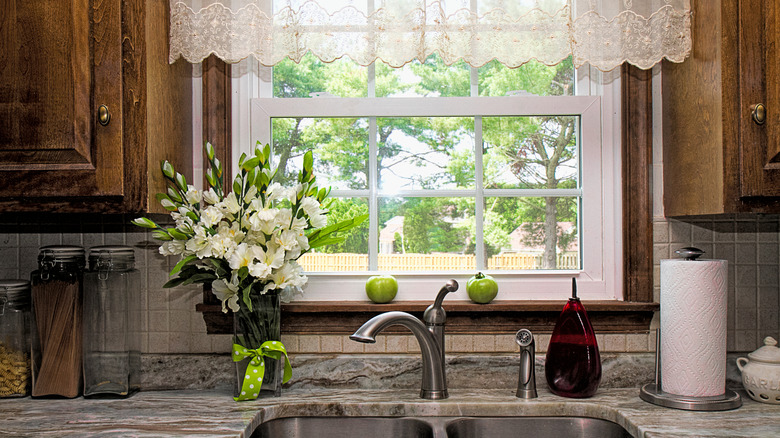 View of a kitchen sink, window view of backyard, valances and flowers.