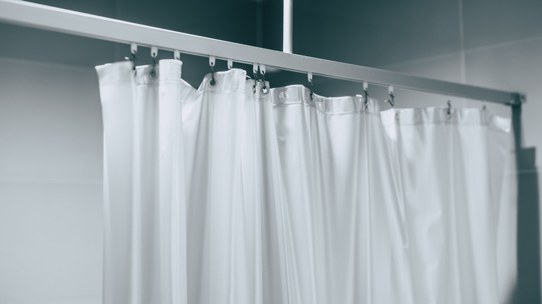 A white plastic shower curtain hanging on black hooks