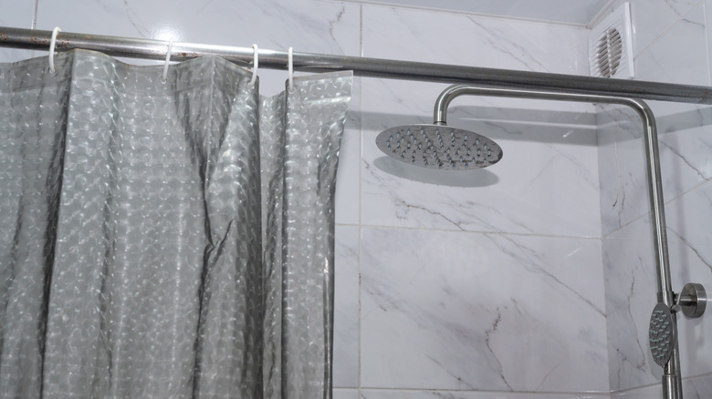 A transparent shower curtain liner hanging on white rings