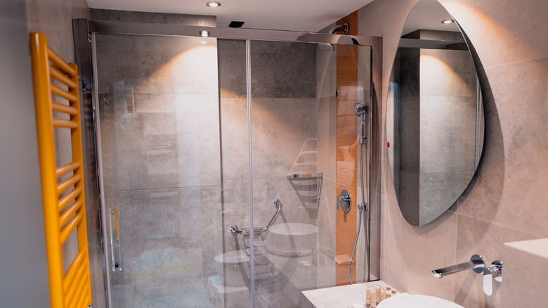 A modern bathroom with a glass shower and large round mirror