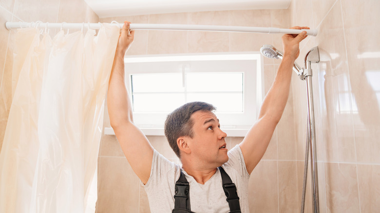 A man installing a white shower curtain on a tension rod
