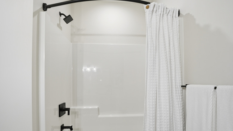 A white textured shower curtain hanging on a black rod in a white bathroom