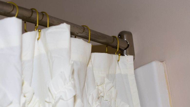 A white shower curtain hanging on gold metal rings
