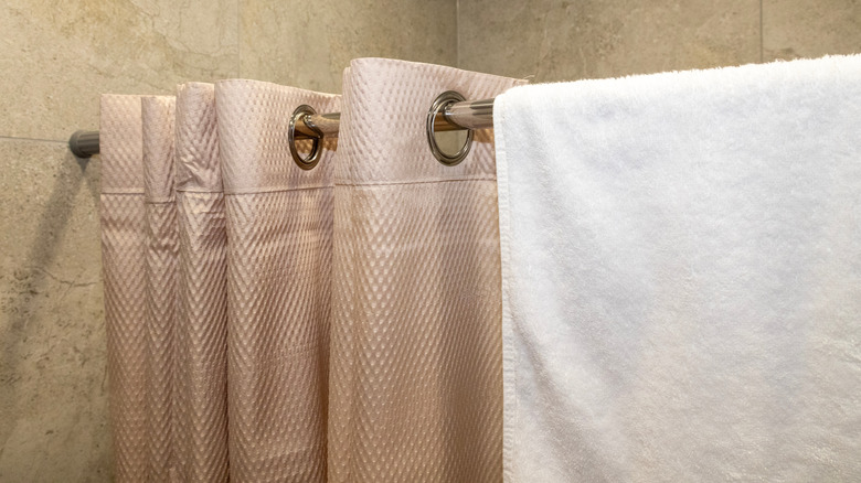 A bunched up tan shower curtain hanging on a rod next to a white towel