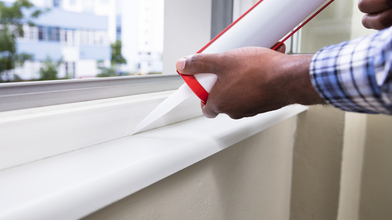 A person caulks around their window frame