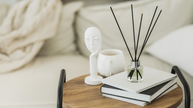 Minimalist side table setup with fragrance sticks on books, statue, and coffee mug