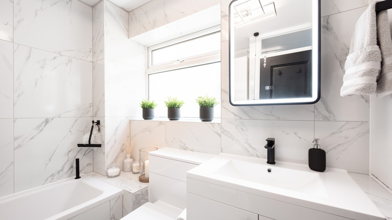 A general interior view of a newly fitted white bathroom with marble effect wall tiles and black accessories.