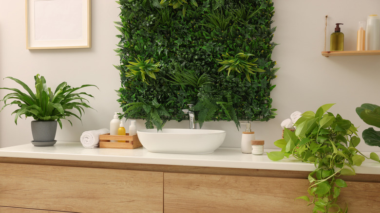 Green artificial plants, vanity and different personal care products in bathroom