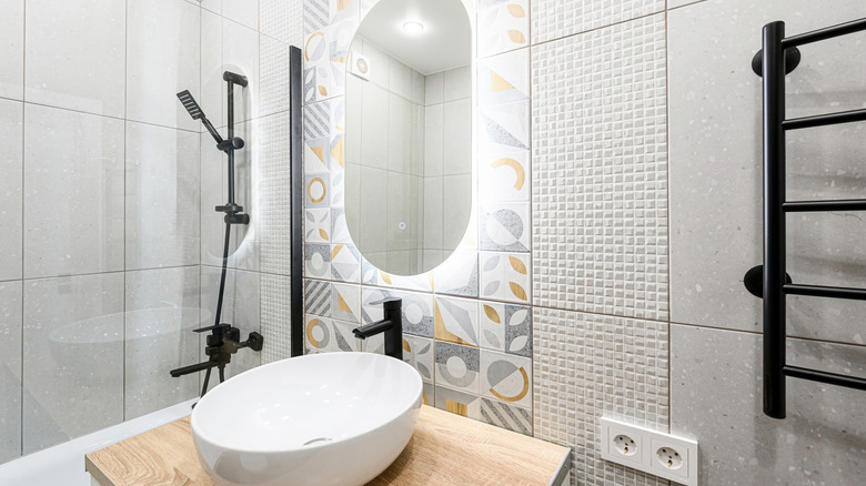 Modern bathroom featuring a white oval sink on a wood countertop, a black faucet and shower fixtures, decorative tiles, and an illuminated mirror